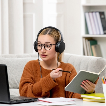 student online cute girl in glasses and sweater studying on computer writing down notes